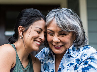 Two woman in front of house with their heads together